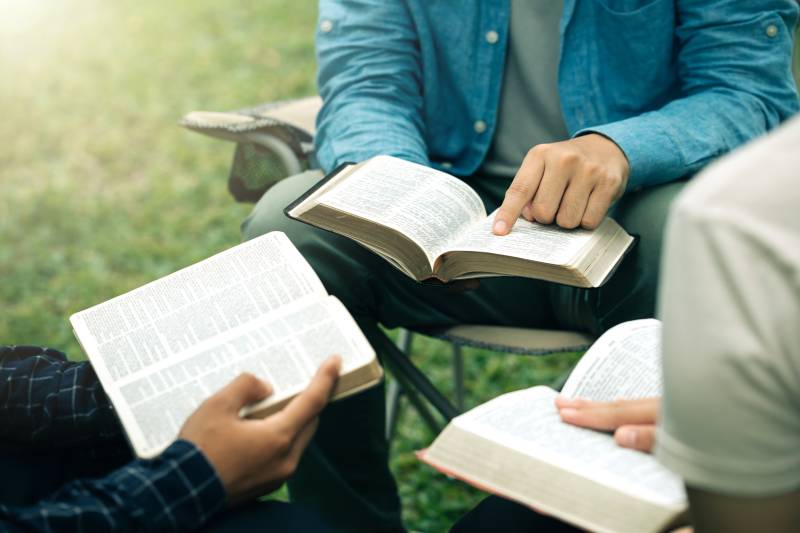 Christian group read and studied the bible at the park and prayed together. sharing the gospel with a friend. Holy Bible study reading together on Sunday. Study the Word Of God With Friends. Education